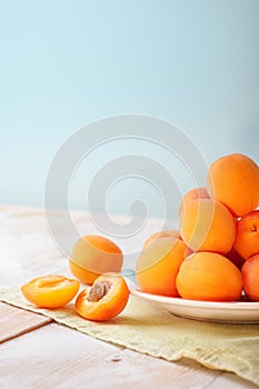 Vertical photo of Delicious ripe orange apricots in a bright plate on wooden table with green napkin on light blue wall background