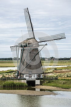 Vertical photo of the polder windmill `Het Noord` on wadden sea island Texel in the Netherlands with a blue sky and some clouds