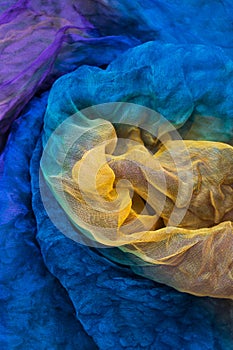 A vertical photo of fabric dyed yellow, blue, purple colours and laid out in an abstract form for use as a background