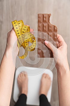 Vertical photo female hands hold chocolate and measuring tape concept of what is