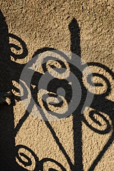 Vertical photo of fence shadows with curls on concrete wall