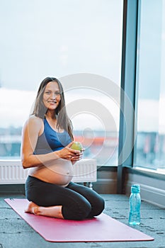 Vertical photo fitness athletic beauteous pregnant woman in sportswear top, leggings. Doing yoga, sitting on bent legs