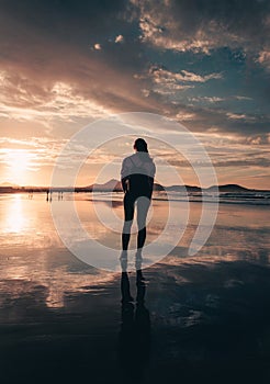 Vertical photo of free woman tourist on the beach during the sunset golden hour looking at the ocean. Woman on the beach with her