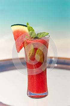 Vertical photo of fresh watermelon juice with mint on the glass table ocean background at the beach