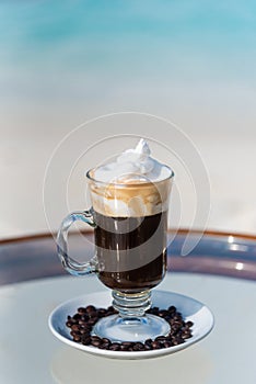 Vertical photo of the freshly made black coffee cocktail on the glass table at the beach with ocean