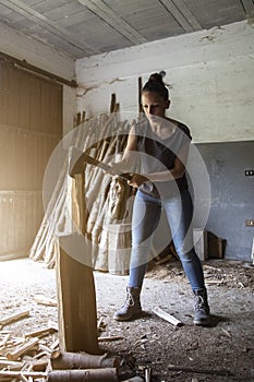 Vertical photo of a girl concentrating on splitting firewood with an axe in her hands to store and make fire in winter. rural life