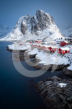 Vertical photo of Hamnoy fishing village in Norway. Lofoten winter scene with typical red houses and a snowy mountain.