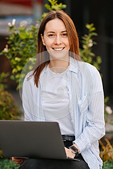 Vertical photo of happy casual young woman working on laptop remote outdoor