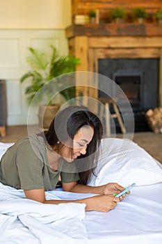 Vertical photo of a happy laughing Asian woman lies in bed with mobile phone. She received a declaration of love from