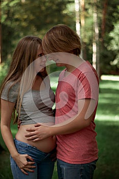 Vertical photo. A happy married couple Husband hugs a beautiful adult pregnant wife. walks in a park. Second trimester.