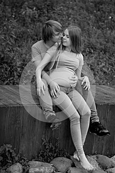 Vertical photo. A happy married couple Husband hugs a beautiful adult pregnant wife. walks in a park. Second trimester.