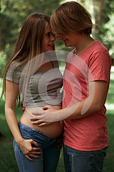 Vertical photo. A happy married couple Husband hugs a beautiful adult pregnant wife. walks in a park. Second trimester.