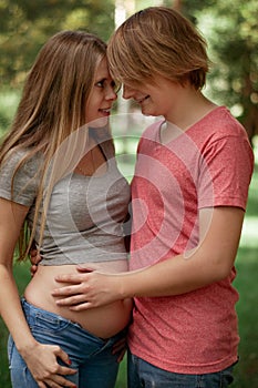 Vertical photo. A happy married couple Husband hugs a beautiful adult pregnant wife. walks in a park. Second trimester.