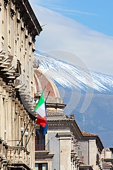 Vertical photo of historical building in Sicilian Catania, Italy with waving Italian flag on the facade. In background cupola of