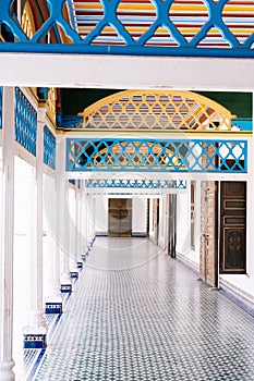 Vertical photo of an inner courtyard with different doors and columns with metal arches and colored tiles on the floor