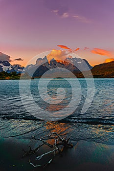 Vertical photo of a lake with some rocky snowy peaks of a mountain with the sun coming out behind