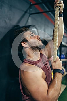 Vertical photo of a man climbing a rope in a gym