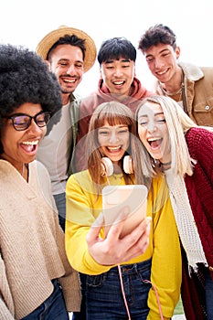Vertical photo. Multicultural group of friends using cell phones and laughing - Cheerful students lined up and