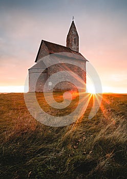 Vertikálna fotografia starého rímskokatolíckeho kostola sv. Michala Archanjela pri západe slnka - Dražovce, Slovensko