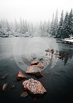 Vertikální fotografie klidného a tichého zamrzlého jezera s kameny na povrchu v zimním období. Zasněžené mlžné jezero Tatliak