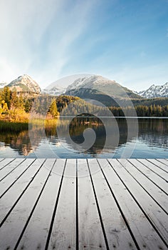 Vertical photo - pier on the lake in autumn scenery and beautiful and snowy mountains on background. Strbske pleso in High Tatras