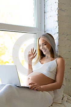 Pregnant woman sits at home in front of a laptop monitor - online consultation with a doctor or online meeting with