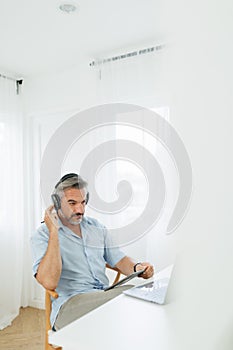 Vertical photo of Serious Senior adult Man in headphones using digital tablet and laptop