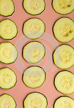 Fifteen round courgette slices with seeds and pulp on a pink background