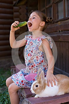 Vertical photo of a six year old girl with a rabbit and a cucumber