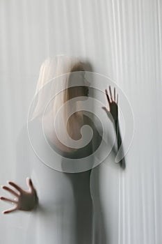 Vertical photo of a slim woman`s silhouette through translucent glass