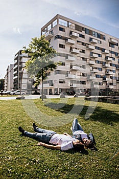 Vertical photo of stylish couple smiling and look at each other lying on green grass