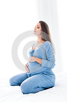 Vertical photo of sweet adorable young mommy sleepwear sitting bed closed eyes imagining future baby indoors apartment