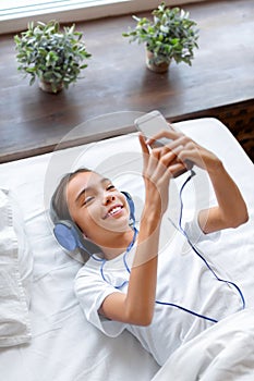 Vertical photo of a teenage girl in bed with a smartphone during an online video call. She communicates with her friends