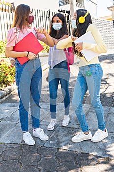 Vertical photo of three teenage Latinx friends with masks waving their elbows at back to school for the prevention of coronavirus photo