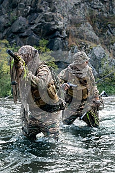 Vertical photo of a two mercenary soldiers ford a river during a sabotage operation.