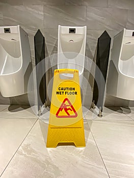 Vertical photo of wet floor alert sign in public male toilet