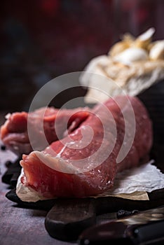 Detail of whole pork tenderloin meat on vintage board with garlic and tomatoes