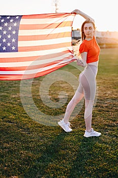 Vertical Photo Woman in Red Sports Top, Tights Holding American Flag Waving in Wind in Full Length