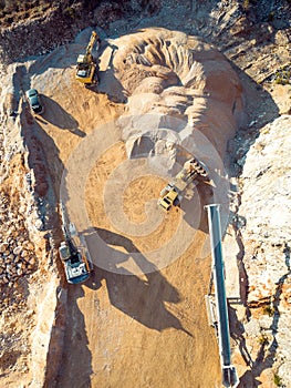 Vertical photo of yellow heavy machinery, excavators working on dusty quarry grounds