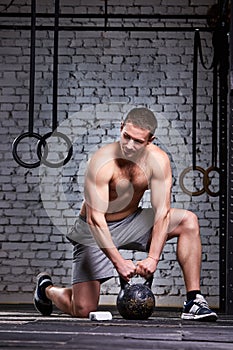 Vertical photo of young athletic man while holding kettlebell on the gym floor against brick wall.