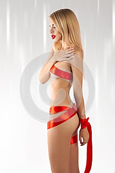 Vertical photo of young beautiful blonde with red ribbons of slim body