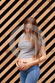 Vertical photo. Young beautiful and happy pregnant girl on a striped background. Second trimester Holds his hands on his stomach.