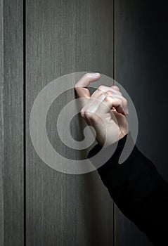 Vertical photo. A young man in a black jacket knocks on the door. A visit to someone's home. Knock on the wooden door.