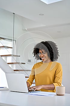 Happy African American young woman using laptop sitting at home table. Vertical