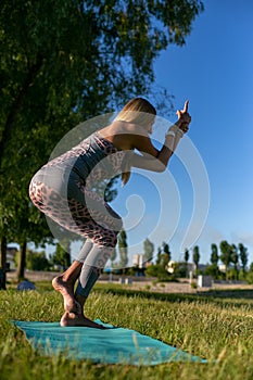 Vertical photo of a young woman standing in an asana on a background of nature
