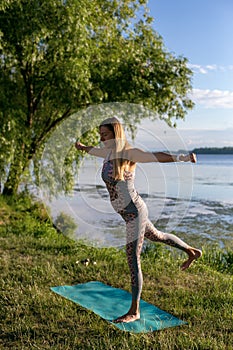Vertical photo of a young woman standing in an asana by the river