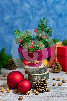 Vertical photograph of coniferous branches in a vase wrapped in red paper, on wooden stands.