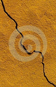 Vertical photograph of a dark-yellow painted wall with a large crack from top to bottom