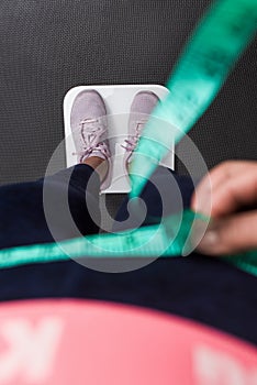 Vertical photography close up woman measuring waist, focus on the sneakers at the white scale