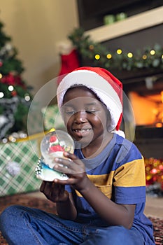 Vertical picture of african american boy holding christmas snowing ball and siting next fireplace